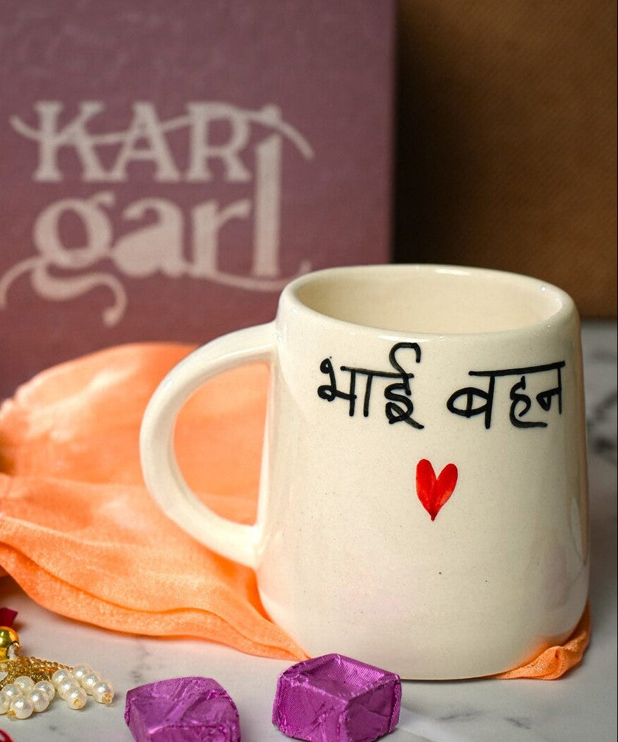 White mug with text, marigold flowers, and decorative items on a marble surface with 'Kari Garl' box in the background.