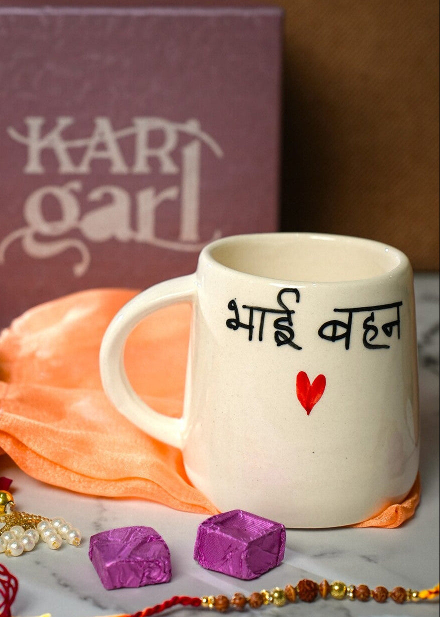 White mug with text, marigold flowers, and decorative items on a marble surface with 'Kari Garl' box in the background.
