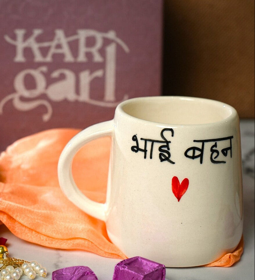 White mug with text, marigold flowers, and decorative items on a marble surface with 'Kari Garl' box in the background.